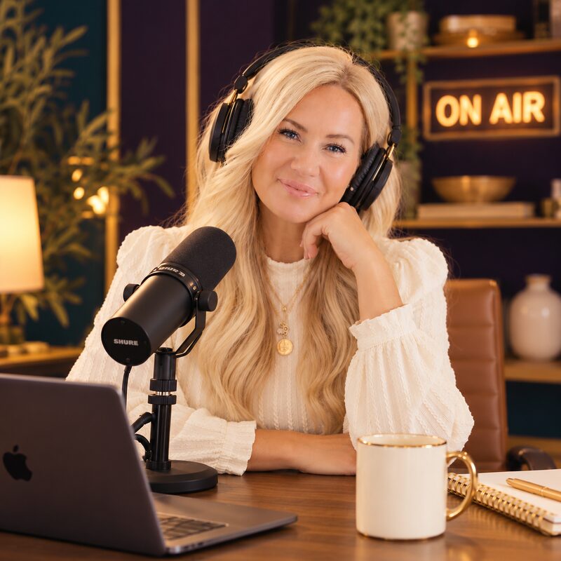 Jana Bishop smiling at her podcast desk, wearing headphones beside a microphone, with a glowing ON AIR sign behind her